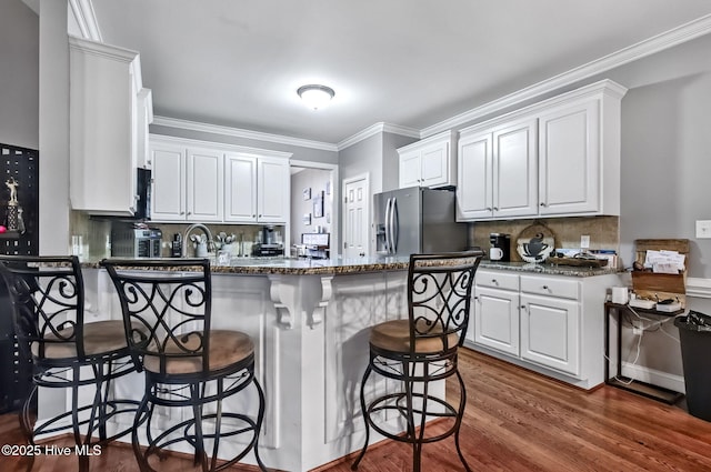 3509 Wales Pl N, Wilson, NC 27896 - kitchen featuring stainless steel fridge with ice dispenser, a peninsula, white cabinetry, a kitchen bar, and crown molding