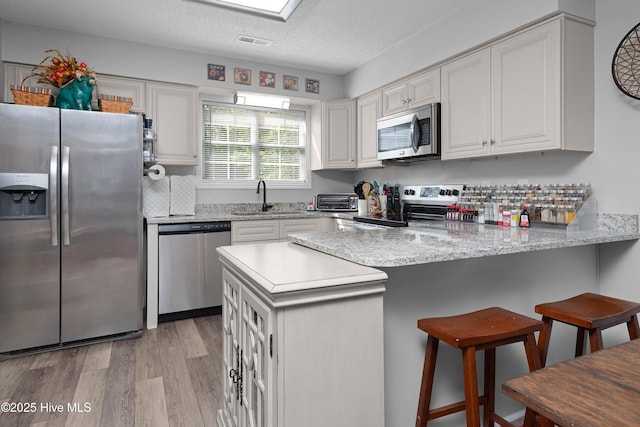 229 Trappers Trl, New Bern, NC 28560 - kitchen with appliances with stainless steel finishes, a peninsula, light wood-style floors, white cabinets, and a kitchen breakfast bar