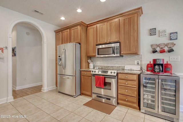 9116 Oak Ridge Plantation Dr, Calabash, NC 28467 - kitchen with appliances with stainless steel finishes, beverage cooler, decorative backsplash, light tile patterned floors, and light stone counters