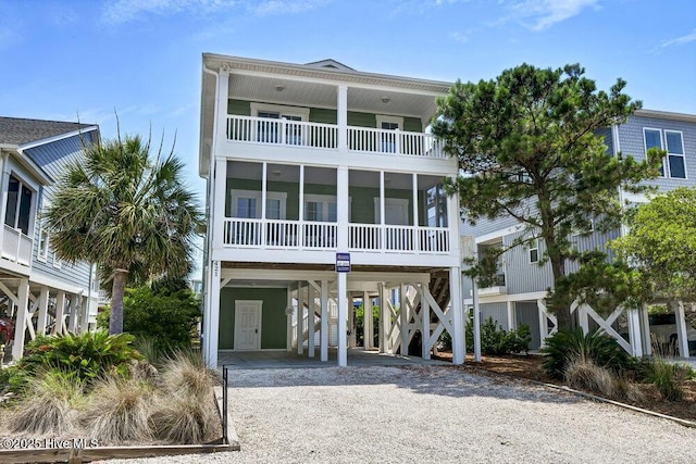 421 30th St, Sunset Beach, NC 28468 - coastal inspired home featuring a carport, a balcony, gravel driveway, and a sunroom