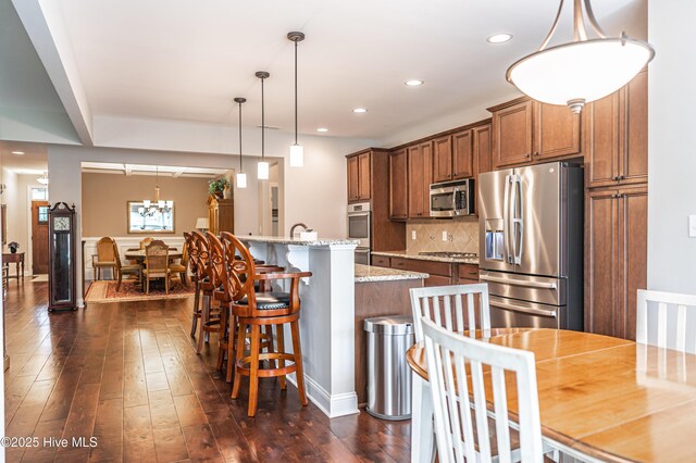 255 Champions Ridge Dr, Southern Pines, NC 28387 - kitchen featuring stainless steel appliances, brown cabinets, a center island with sink, backsplash, and dark wood-style flooring