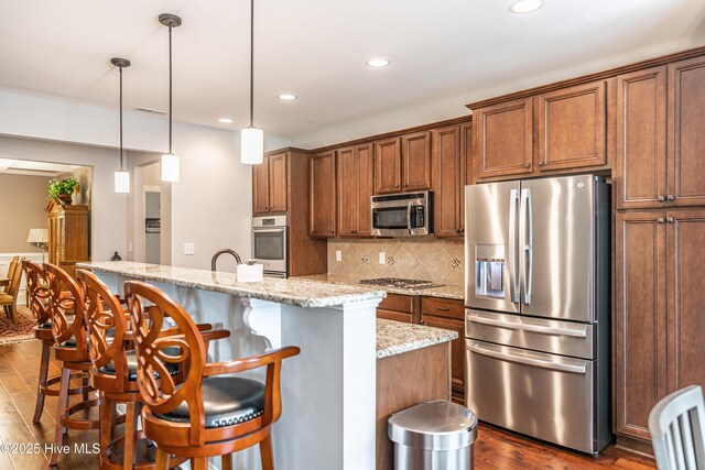 255 Champions Ridge Dr, Southern Pines, NC 28387 - kitchen with appliances with stainless steel finishes, dark wood-style flooring, backsplash, a kitchen breakfast bar, and a center island with sink