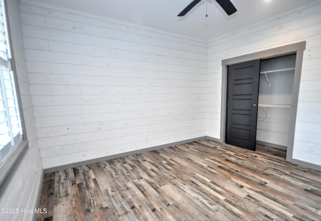9265 W Lake Rd, Calabash, NC 28467 - unfurnished bedroom with wood finished floors, wood walls, a closet, a ceiling fan, and baseboards