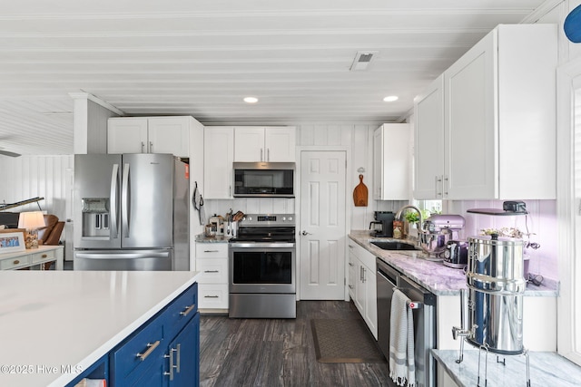 1001 W Beach Dr, Oak Island, NC 28465 - kitchen with stainless steel appliances, blue cabinets, a sink, white cabinetry, and dark wood-style floors