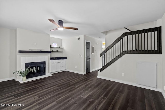 648 Cobblestone Dr, Wilmington, NC 28405 - unfurnished living room featuring ceiling fan, dark wood-style flooring, stairway, a tile fireplace, and baseboards