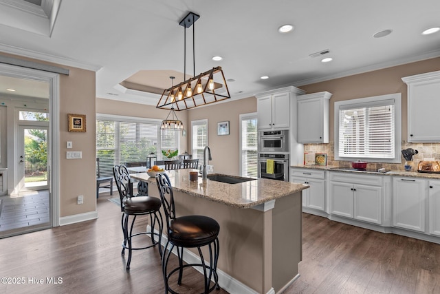2169 Whiskey Branch Dr, Wilmington, NC 28409 - kitchen featuring crown molding, decorative backsplash, dark wood-style floors, a kitchen island with sink, and light stone counters