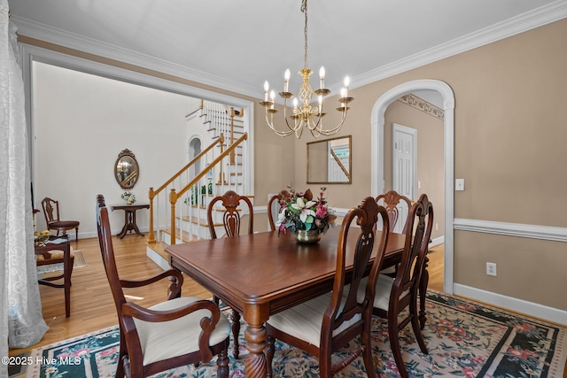 6304 Wolfhead Ct, Wilmington, NC 28411 - dining room featuring stairway, arched walkways, ornamental molding, light wood-style flooring, and a chandelier
