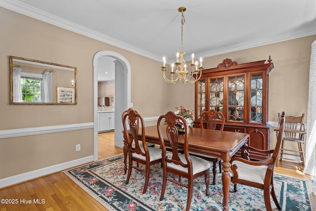 6304 Wolfhead Ct, Wilmington, NC 28411 - dining area featuring a chandelier, arched walkways, light wood-style flooring, ornamental molding, and baseboards