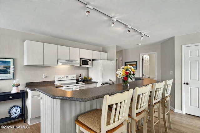 816 Colony Pl Unit D, Sunset Beach, NC 28468 - kitchen with white appliances, under cabinet range hood, dark countertops, rail lighting, and light wood-style flooring