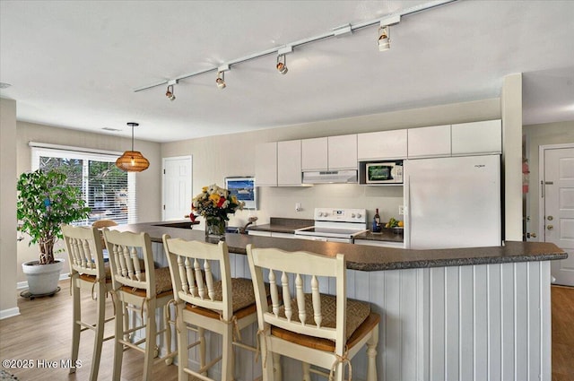 816 Colony Pl Unit D, Sunset Beach, NC 28468 - kitchen with white appliances, under cabinet range hood, dark countertops, rail lighting, and light wood-style floors