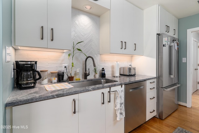 185 Ponte Vedra Dr, Pinehurst, NC 28374 - kitchen with appliances with stainless steel finishes, dark stone counters, light wood finished floors, white cabinets, and backsplash