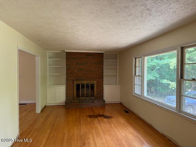 430 W Rhode Island Ave, Southern Pines, NC 28387 - unfurnished living room featuring a textured ceiling, wood finished floors, built in shelves, a fireplace, and baseboards