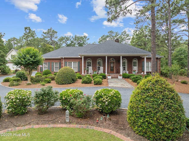 155 Mckenzie Rd E, Pinehurst, NC 28374 - neoclassical home featuring a porch, brick siding, a chimney, and roof with shingles