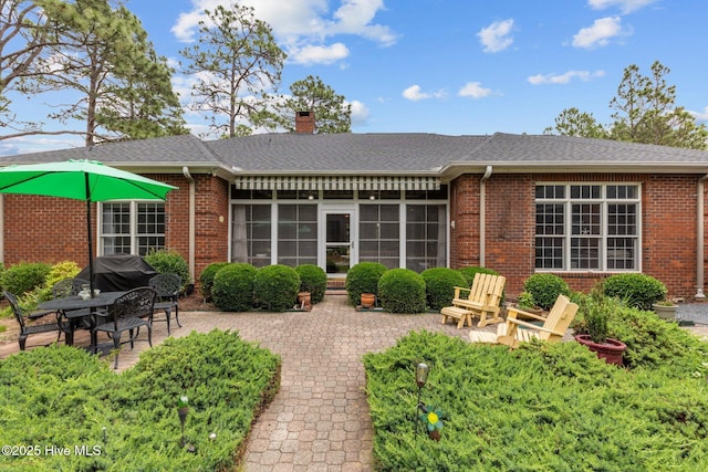 155 Mckenzie Rd E, Pinehurst, NC 28374 - back of house featuring brick siding, a chimney, a patio area, a sunroom, and a shingled roof