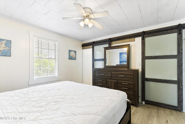 805 Carolina Beach Ave N, Carolina Beach, NC 28428 - bedroom featuring ornamental molding, a barn door, light wood-type flooring, and ceiling fan