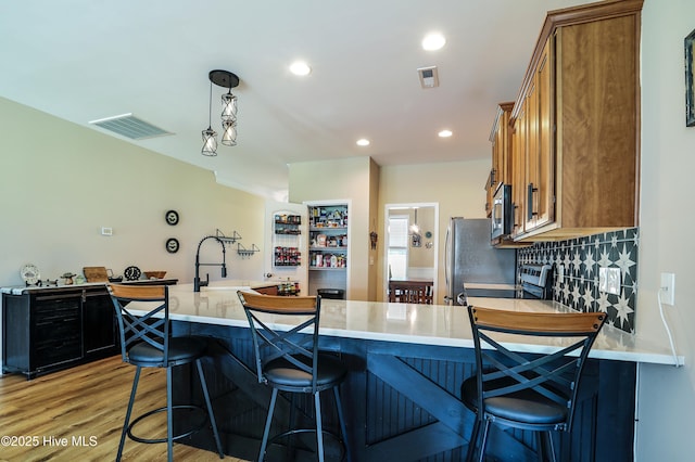 1187 S Brook Rd, Winnabow, NC 28479 - kitchen with brown cabinetry, stainless steel appliances, light wood-type flooring, a kitchen bar, and recessed lighting