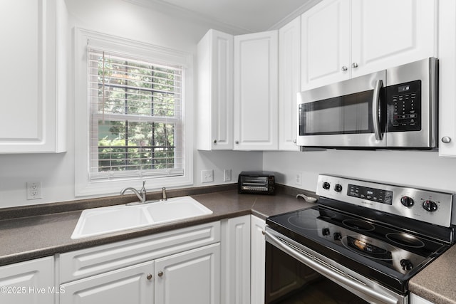 2555 St James Dr SE Unit 102, Southport, NC 28461 - kitchen featuring stainless steel appliances, a sink, dark countertops, white cabinets, and ornamental molding
