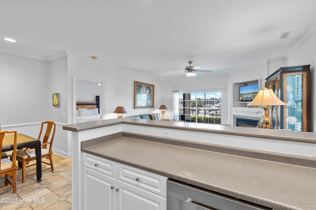 2555 St James Dr SE Unit 102, Southport, NC 28461 - kitchen with dishwasher, ornamental molding, a ceiling fan, white cabinetry, and a glass covered fireplace