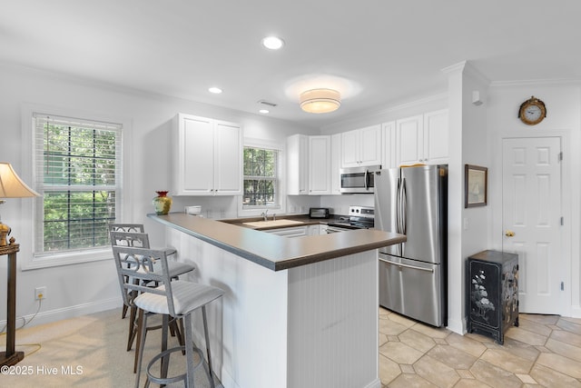2555 St James Dr SE Unit 102, Southport, NC 28461 - kitchen with stainless steel appliances, a kitchen breakfast bar, white cabinets, a peninsula, and crown molding