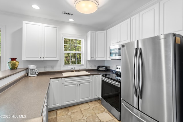 2555 St James Dr SE Unit 102, Southport, NC 28461 - kitchen with stainless steel appliances, a sink, white cabinets, dark countertops, and crown molding