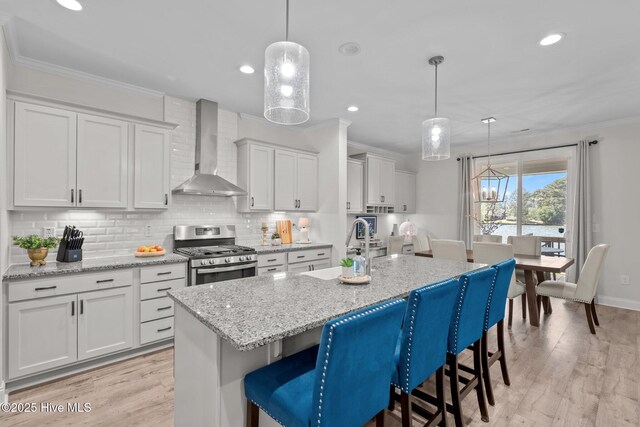 106 Josephs Pt, West End, NC 27376 - kitchen featuring stainless steel gas range, wall chimney exhaust hood, backsplash, crown molding, and a kitchen island with sink