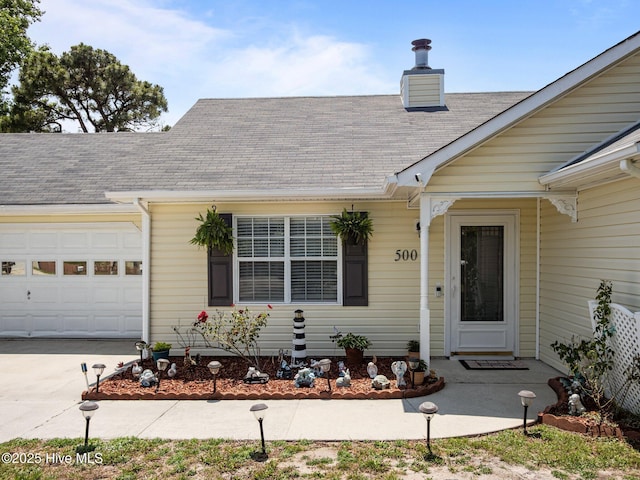 500 Nutfield Dr, Hubert, NC 28539 - view of exterior entry featuring a garage, a shingled roof, concrete driveway, and a chimney