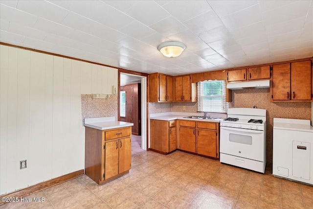 110 Texanna Ln, Raeford, NC 28376 - kitchen with white range with gas stovetop, brown cabinetry, under cabinet range hood, light countertops, and a sink