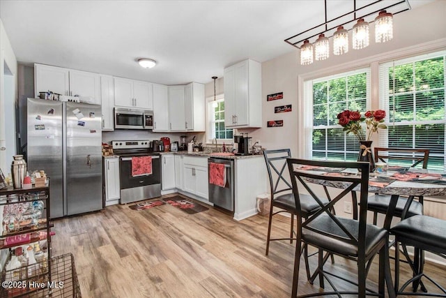 209 Bunche Dr, Goldsboro, NC 27530 - kitchen with stainless steel appliances, light wood finished floors, a sink, white cabinets, and decorative light fixtures