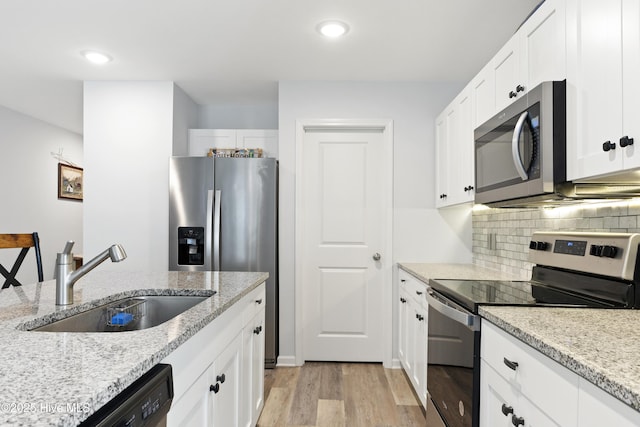 940 Pine Needles Rd, Southport, NC 28461 - kitchen featuring appliances with stainless steel finishes, a sink, light wood-type flooring, white cabinetry, and decorative backsplash