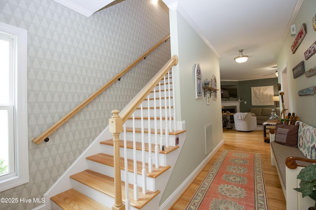 305 3rd St, Aberdeen, NC 28315 - staircase with wallpapered walls, crown molding, wood finished floors, a fireplace, and ceiling fan