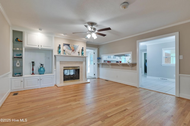 unfurnished living room with light wood-style floors, a ceiling fan, a high end fireplace, crown molding, and plenty of natural light