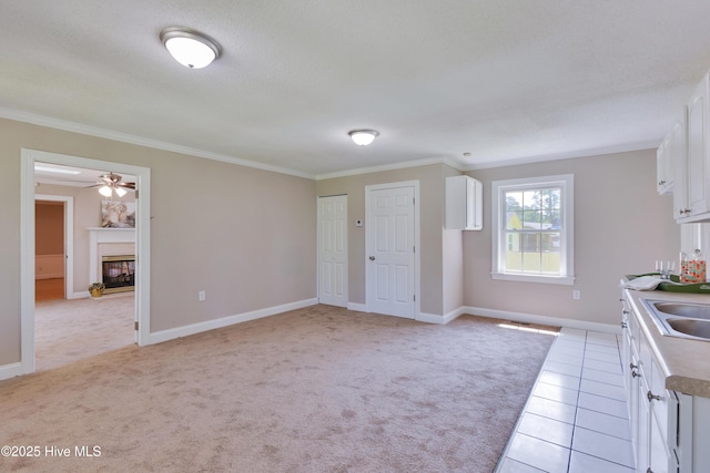 kitchen with ornamental molding, white cabinets, a glass covered fireplace, ceiling fan, and baseboards