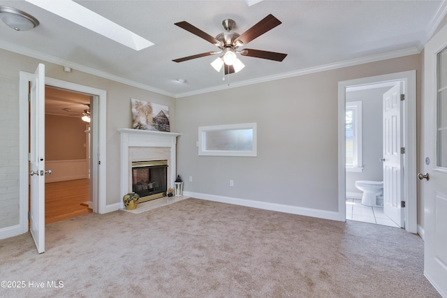 unfurnished living room featuring carpet flooring, crown molding, a fireplace, ceiling fan, and a skylight