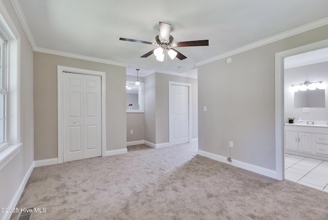unfurnished bedroom with multiple closets, light colored carpet, ornamental molding, ensuite bath, and baseboards