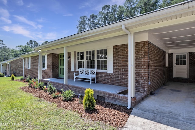 view of property exterior with a porch, brick siding, a carport, and driveway
