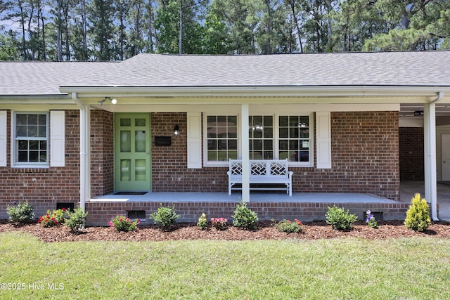 view of front of home with covered porch, roof with shingles, a front yard, and brick siding