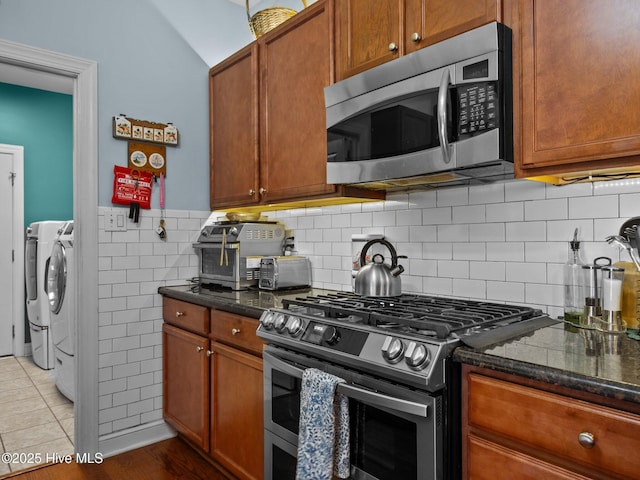 211 Brook Crossing Rd, Swansboro, NC 28584 - kitchen with stainless steel appliances, separate washer and dryer, dark stone countertops, brown cabinetry, and lofted ceiling