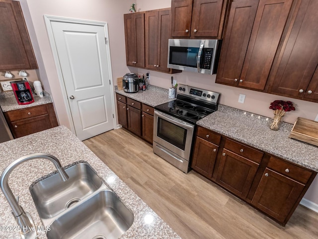 227 Cheswick Dr, Holly Ridge, NC 28445 - kitchen with stainless steel appliances, a sink, light wood-style flooring, light stone counters, and dark brown cabinetry