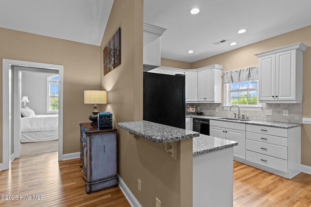 3101 Redfield Dr, Leland, NC 28451 - kitchen with a sink, black appliances, a peninsula, light stone countertops, and white cabinetry