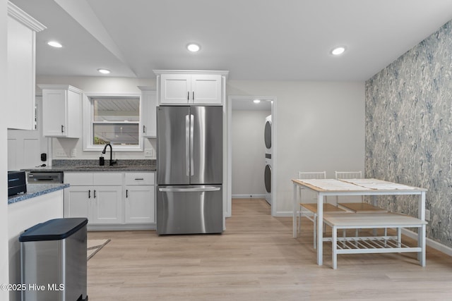 5302 Autumn Dr, Wilmington, NC 28409 - kitchen with freestanding refrigerator, a sink, estacked washer and dryer, white cabinets, and light wood finished floors