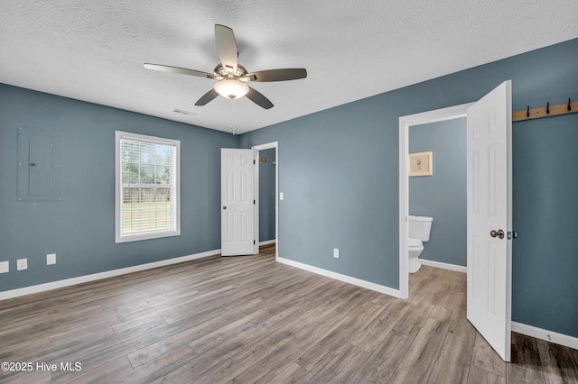 711 Navaho Trl, Wilmington, NC 28409 - unfurnished bedroom featuring wood finished floors, electric panel, a textured ceiling, a ceiling fan, and ensuite bathroom