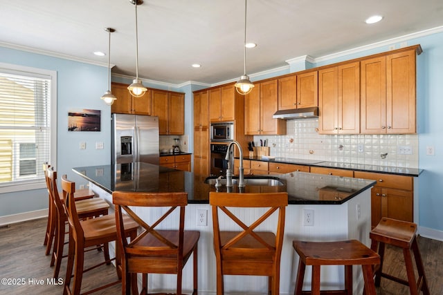 kitchen featuring appliances with stainless steel finishes, under cabinet range hood, brown cabinets, dark wood-style flooring, and ornamental molding
