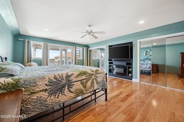 bedroom featuring access to exterior, light wood finished floors, recessed lighting, ceiling fan, and a glass covered fireplace