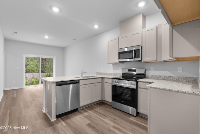 776 Palm Frond Way Unit 55, Calabash, NC 28467 - kitchen with stainless steel appliances, a sink, a peninsula, light wood-type flooring, and light stone counters