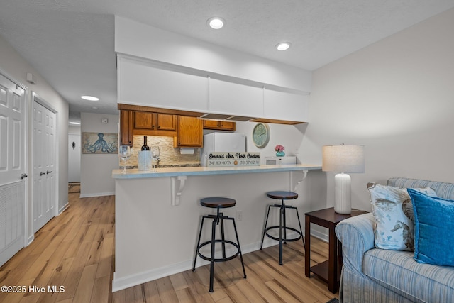 9100 Reed Dr Unit 3107, Emerald Isle, NC 28594 - kitchen with brown cabinetry, a kitchen bar, backsplash, light wood-type flooring, and recessed lighting