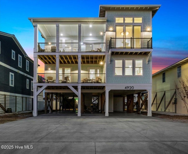 4920 E Beach Dr, Oak Island, NC 28465 - back of house at dusk featuring a carport, a balcony, and concrete driveway