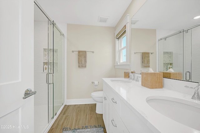 4920 E Beach Dr, Oak Island, NC 28465 - bathroom with wood finished floors, a stall shower, double vanity, baseboards, and toilet