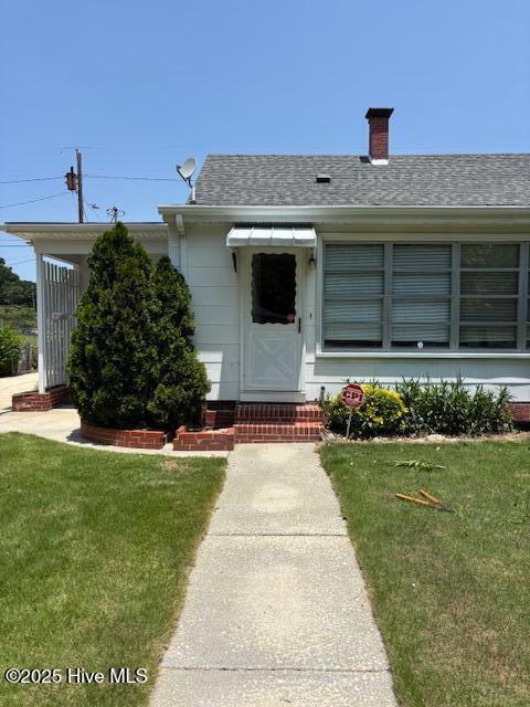 908 E 7th St, Lumberton, NC 28358 - doorway to property with a lawn, a shingled roof, and a chimney