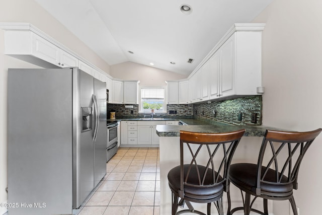 126 NE 5th St, Oak Island, NC 28465 - kitchen featuring stainless steel appliances, a peninsula, dark countertops, vaulted ceiling, and a kitchen bar