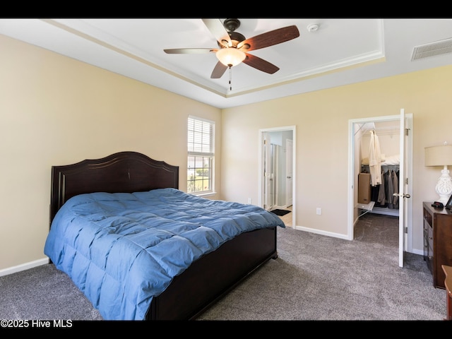 1232 Fence Post Ln, Carolina Shores, NC 28467 - carpeted bedroom featuring a tray ceiling, a spacious closet, baseboards, ceiling fan, and ensuite bathroom